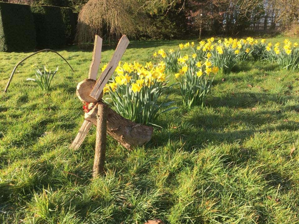 Wooden Easter bunny sitting in grass surrounded by daffodils